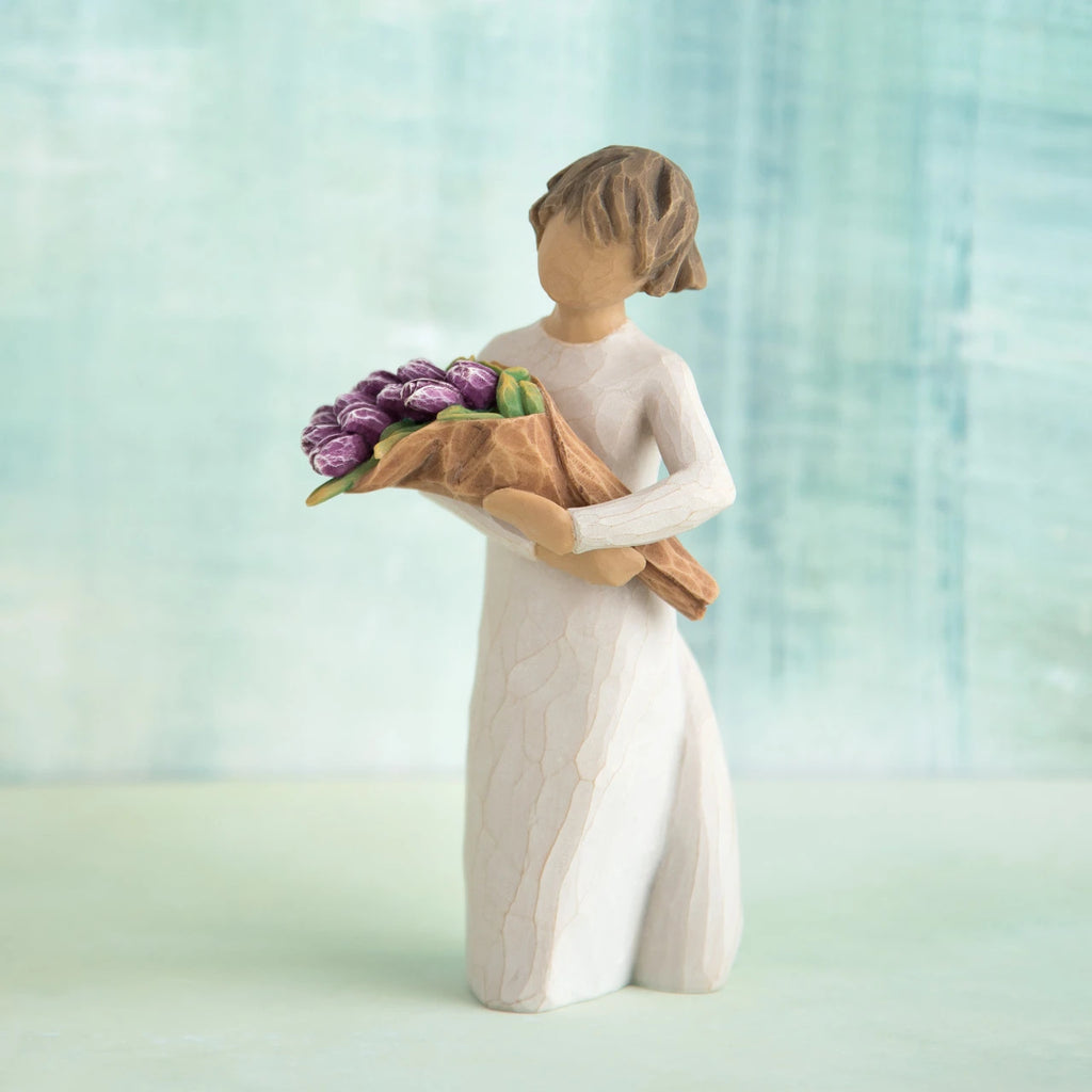 Willow Tree Surprise, 5”h hand-painted standing resin figure in cream dress, holding bouquet of purple tulips, in front of green-blue painting