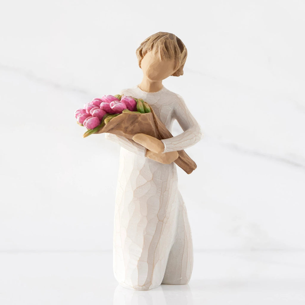 Front view of standing figure in cream dress holding bouquet of pink tulips