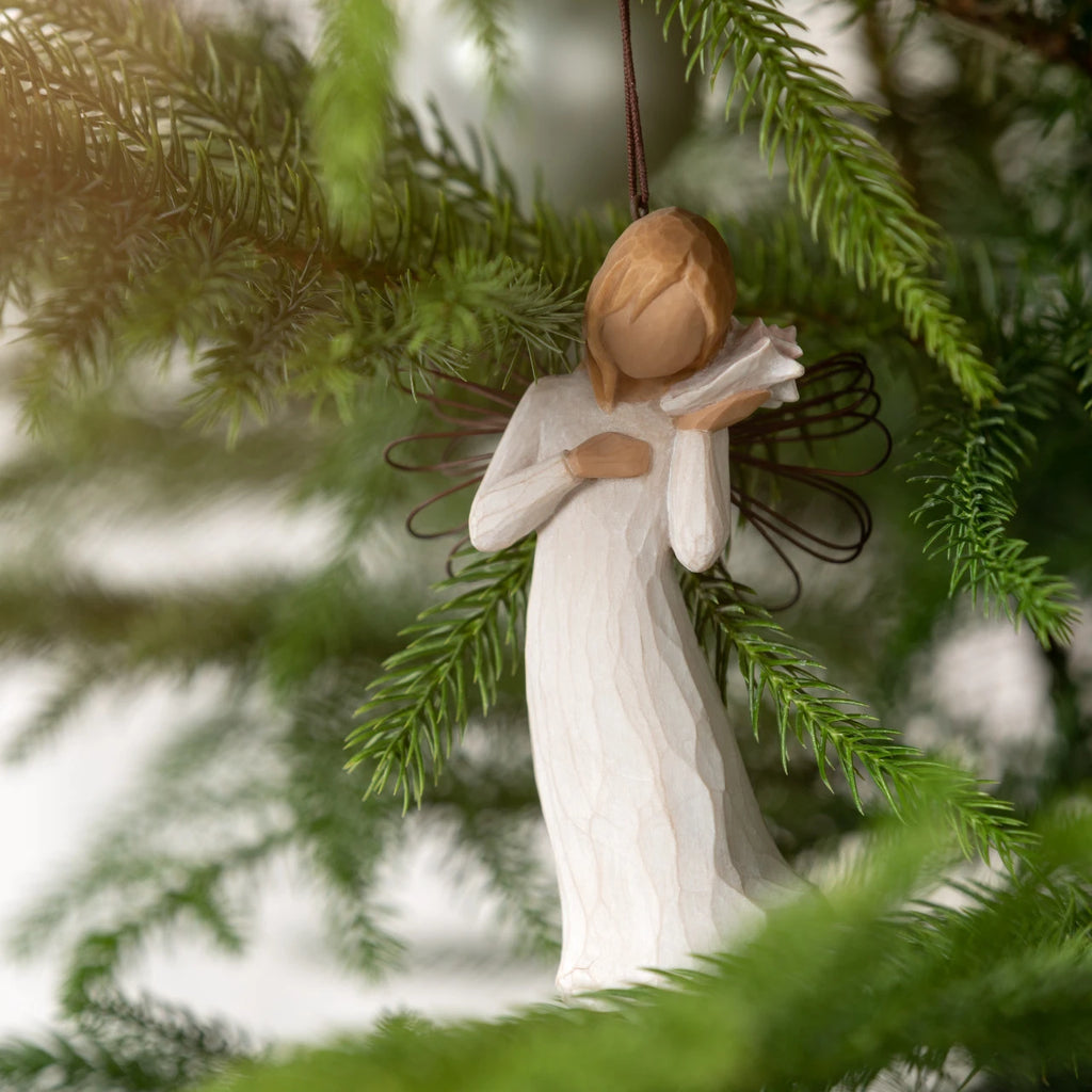 Willow Tree Thinking of You Ornament, 4.5”h hand-painted resin angel figure in cream dress with wire wings, holding pink conch shell to ear, brown elastic cord, hanging on Christmas tree