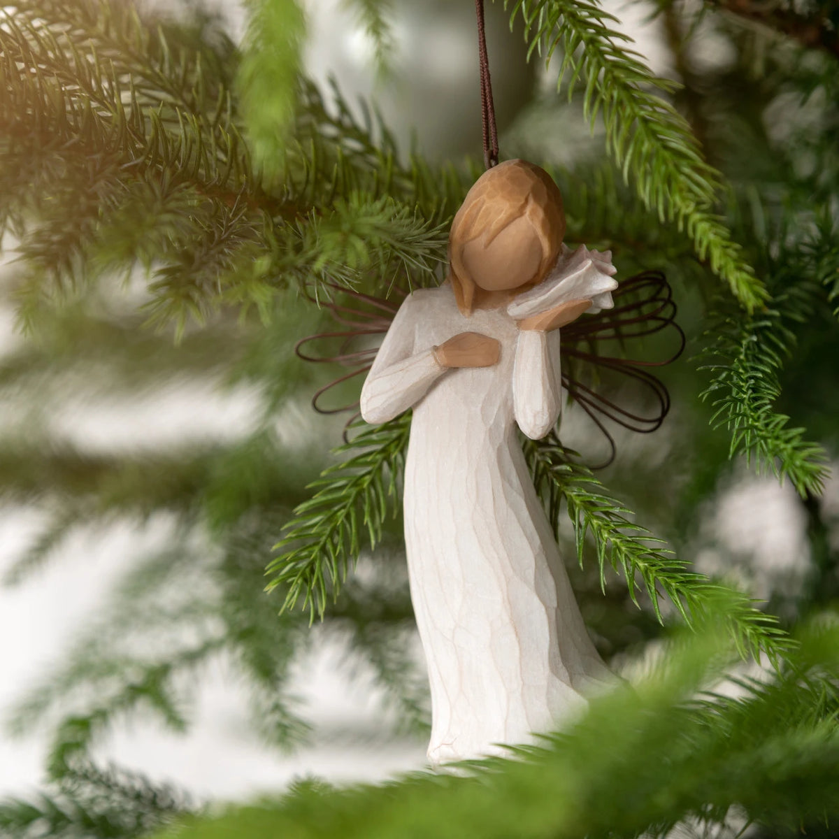 Willow Tree Thinking of You Ornament, 4.5”h hand-painted resin angel figure in cream dress with wire wings, holding pink conch shell to ear, brown elastic cord, hanging on Christmas tree
