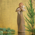 Willow Tree Peace on Earth, 8.5”h hand-painted standing resin figure in gray-green dress, holding baby lamb, in front of ochre painting with fir sprigs