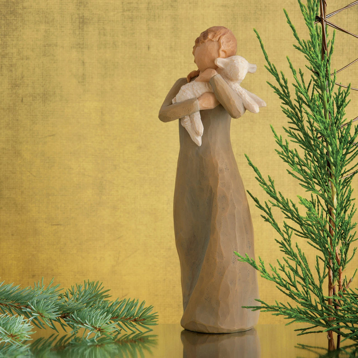 Willow Tree Peace on Earth, 8.5”h hand-painted standing resin figure in gray-green dress, holding baby lamb, in front of ochre painting with fir sprigs