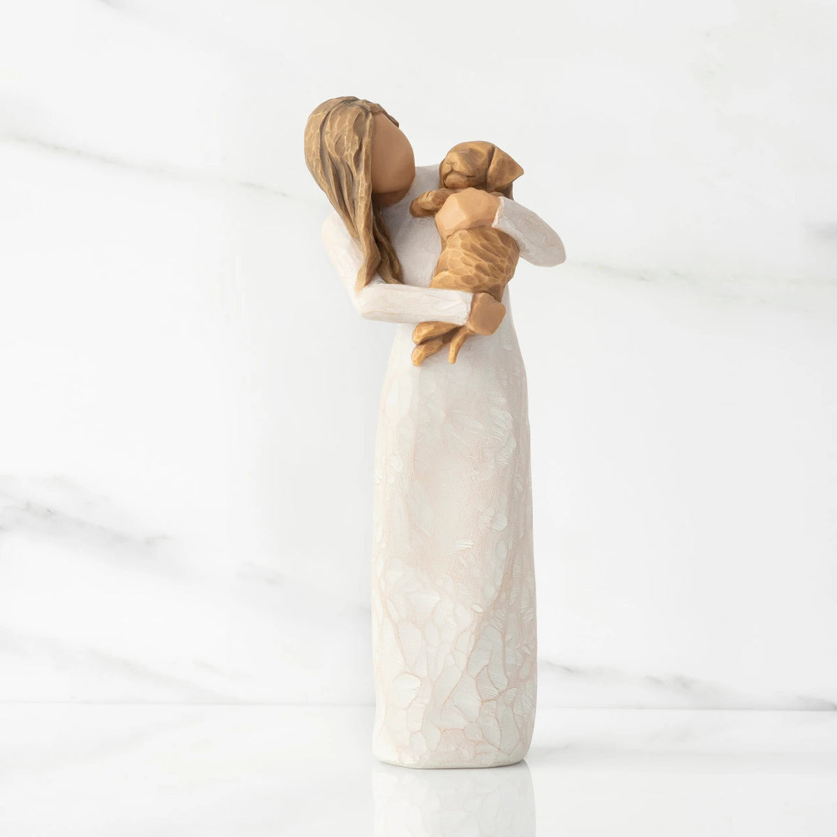 Front view, standing female figure in cream dress, holding golden color puppy in her arms