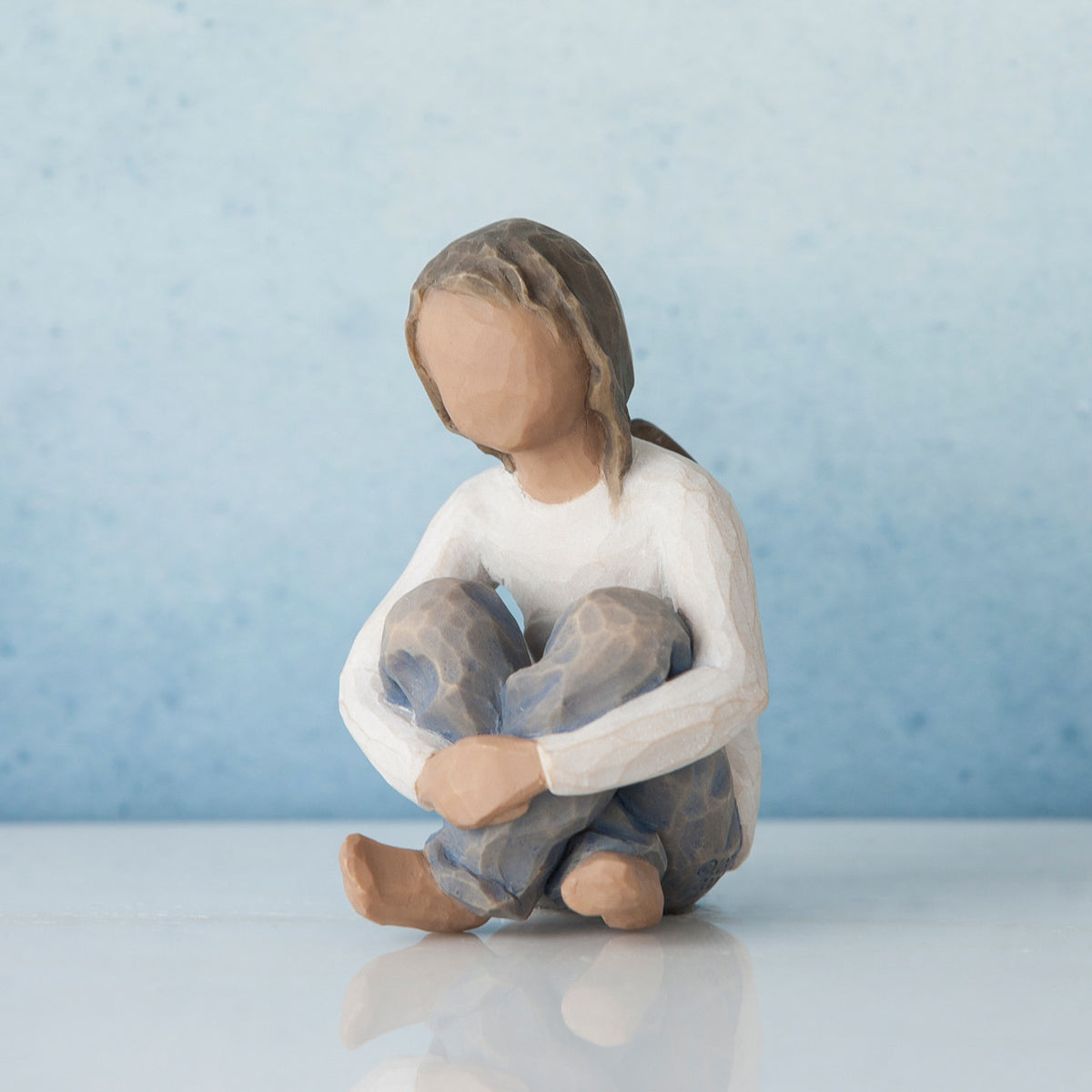 Faceless young girl figurine wearing white shirt and blue jeans sitting with her hands on her knees