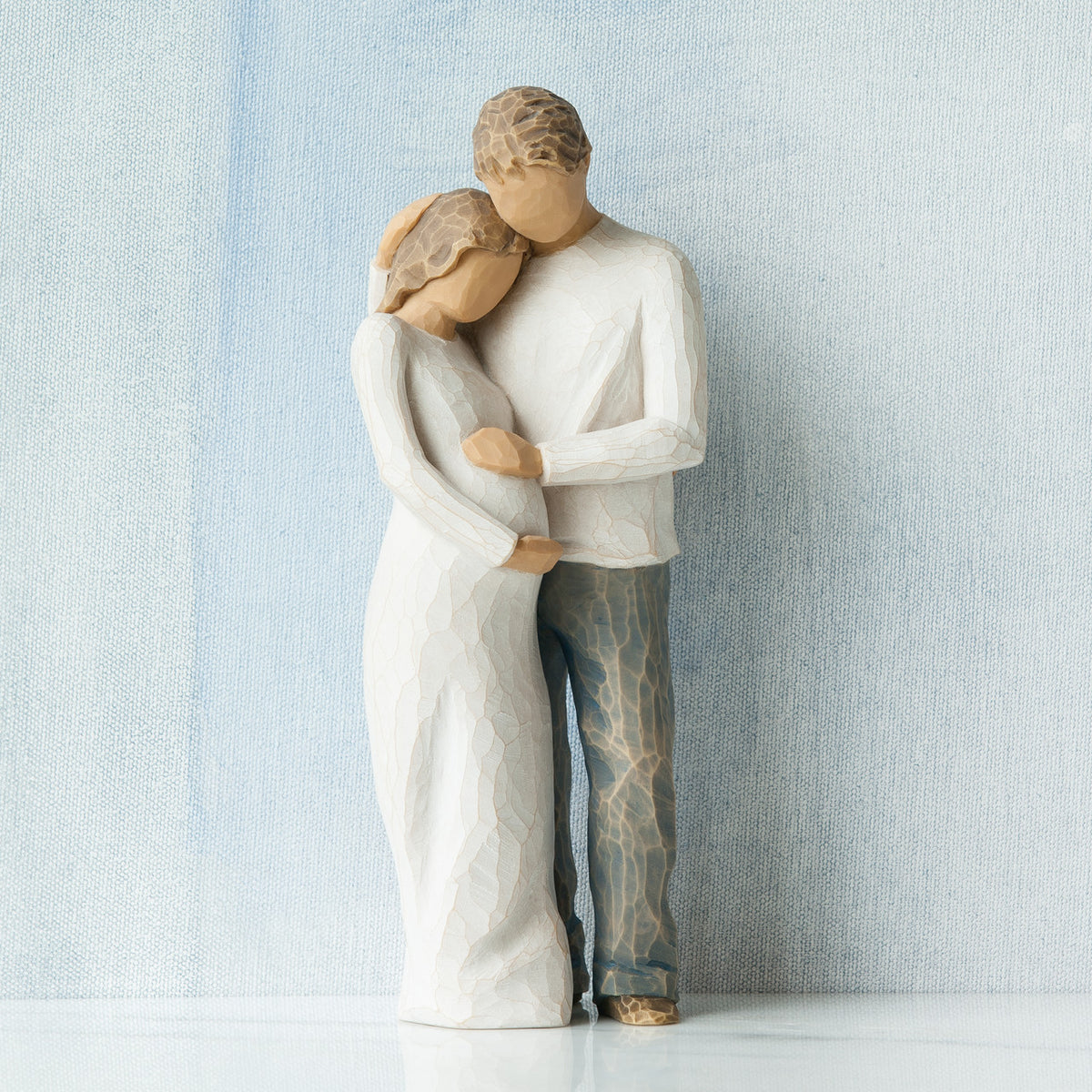 Willow Tree Home, 8.5”h hand-painted standing figure of man and pregnant woman embracing, both in neutral clothes, in front of grey blue painting