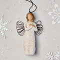 Willow Tree Remembrance Ornament, 4.5”h hand-painted resin angel figure in cream dress carved with symbols of nature, wire wings, crossed hands under small gold-leaf heart, brown elastic cord, laying amongst snowflakes