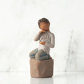 Front view: Figure of darker-skin child, kneeling on rock, holding wire circle with ‘love you’ written in wire