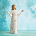 Willow Tree Everyday Blessings, 6.5”h hand-painted standing resin figure with bent elbows and arms raised, cream dress carved with nature symbols and gold-leaf dots, in front of aqua painting