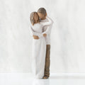 Front view of couple, standing with arms around each other. Woman and man have darker skin tones and hair color.