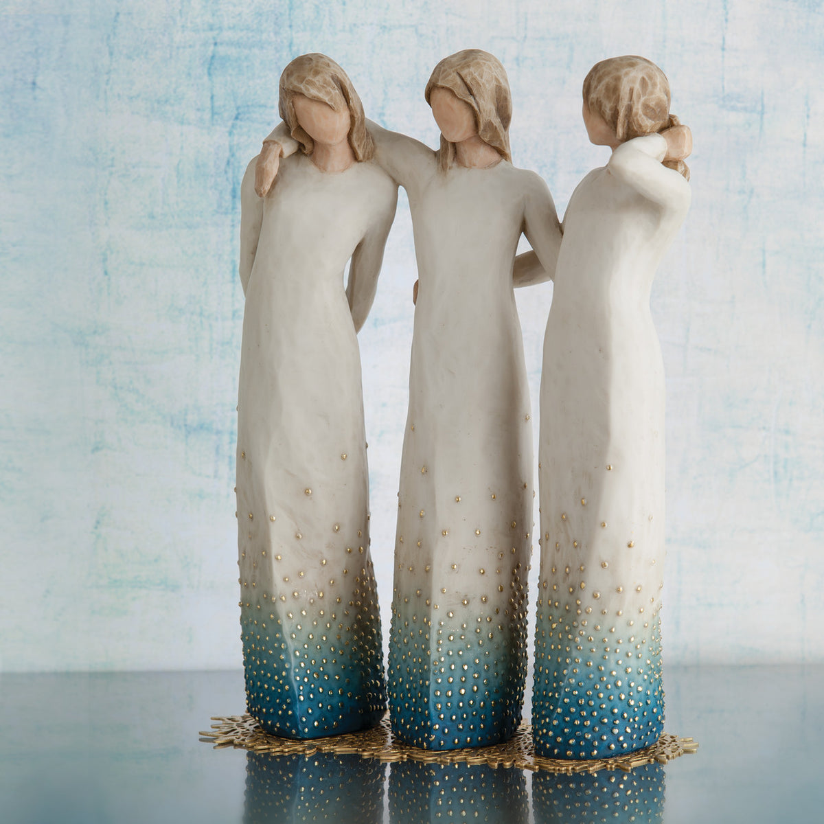 Willow Tree By my side, 9.5" hand-painted resin sculpture of 3 women standing, arms around each other, all in cream and blue ombré dresses with gold-leaf dots, on gold-leaf metal base, in front of pale blue painting