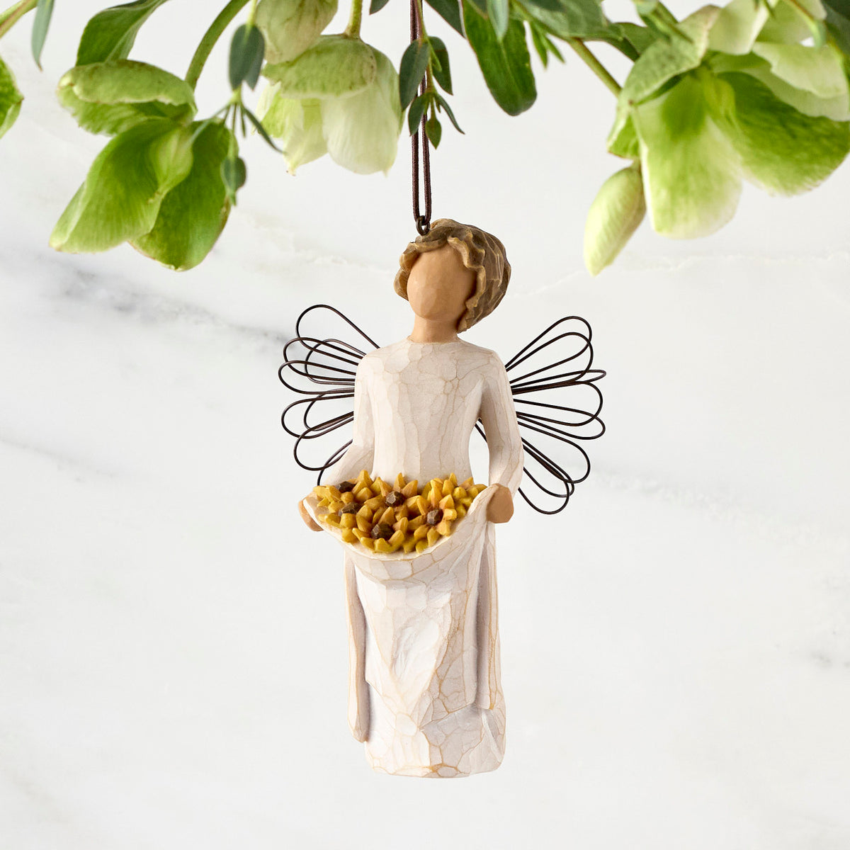 Figure with darker skin, in cream dress with wire wings and wavy brown hair, holding up skirt filled with yellow sunflowers. Hook and loop affixed to figure’s head
