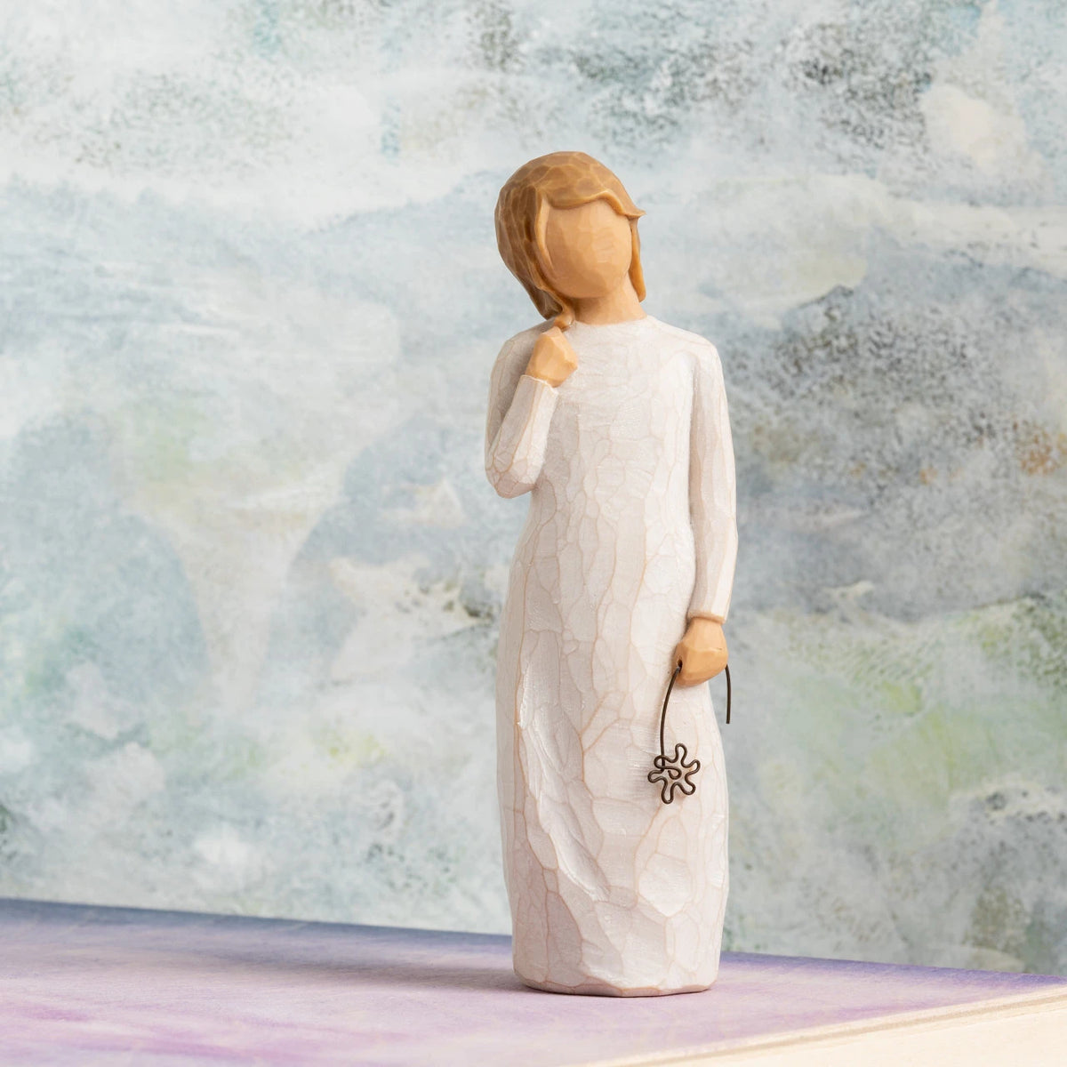 Willow Tree Remember, 5.5”h hand-painted standing resin figure in cream dress holding drooping wire flower in hand, in front of grey painting