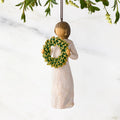 Figure in cream dress, holding green wreath of magnolia leaves in front of her. Hook and loop affixed to figure's head