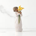Front view of standing figure in cream dress with darker skin holding yellow calla lilies in her arms