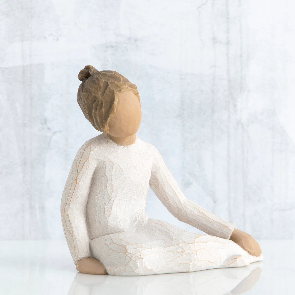 Faceless girl figurine sitting down wearing white dress