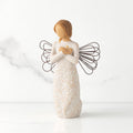 Front view of standing angel in cream dress with wire wings, crossed hands under small gold-leaf heart, dress carved with symbols of nature