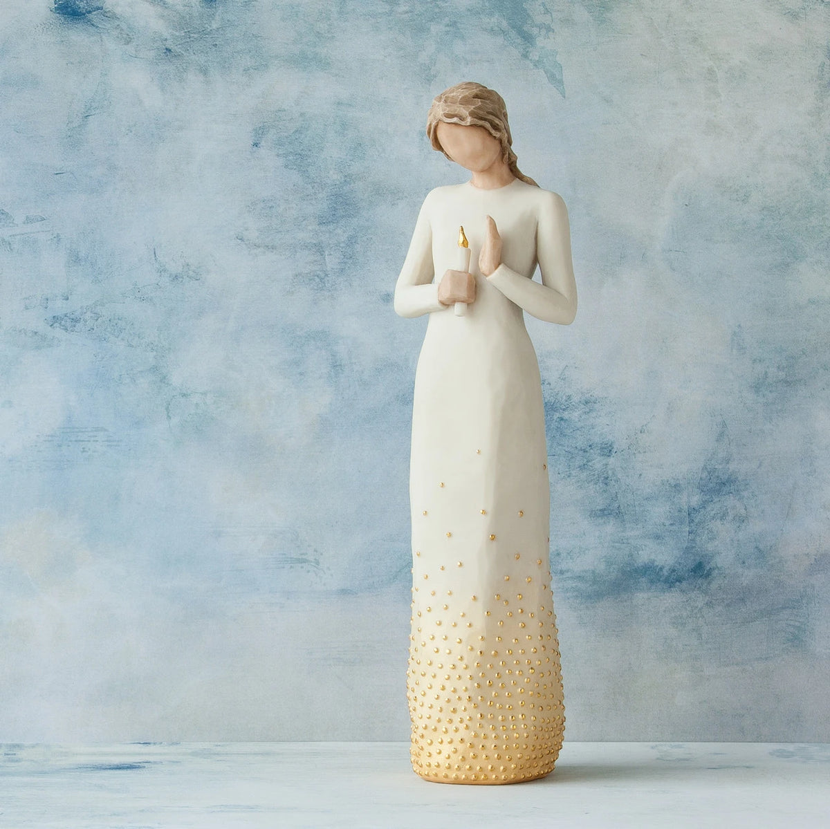 Willow Tree Vigil, 10”h hand-painted standing resin figure in cream dress, holding candleholder with gold candle, skirt embellished with gold-leaf, in front of blue painting