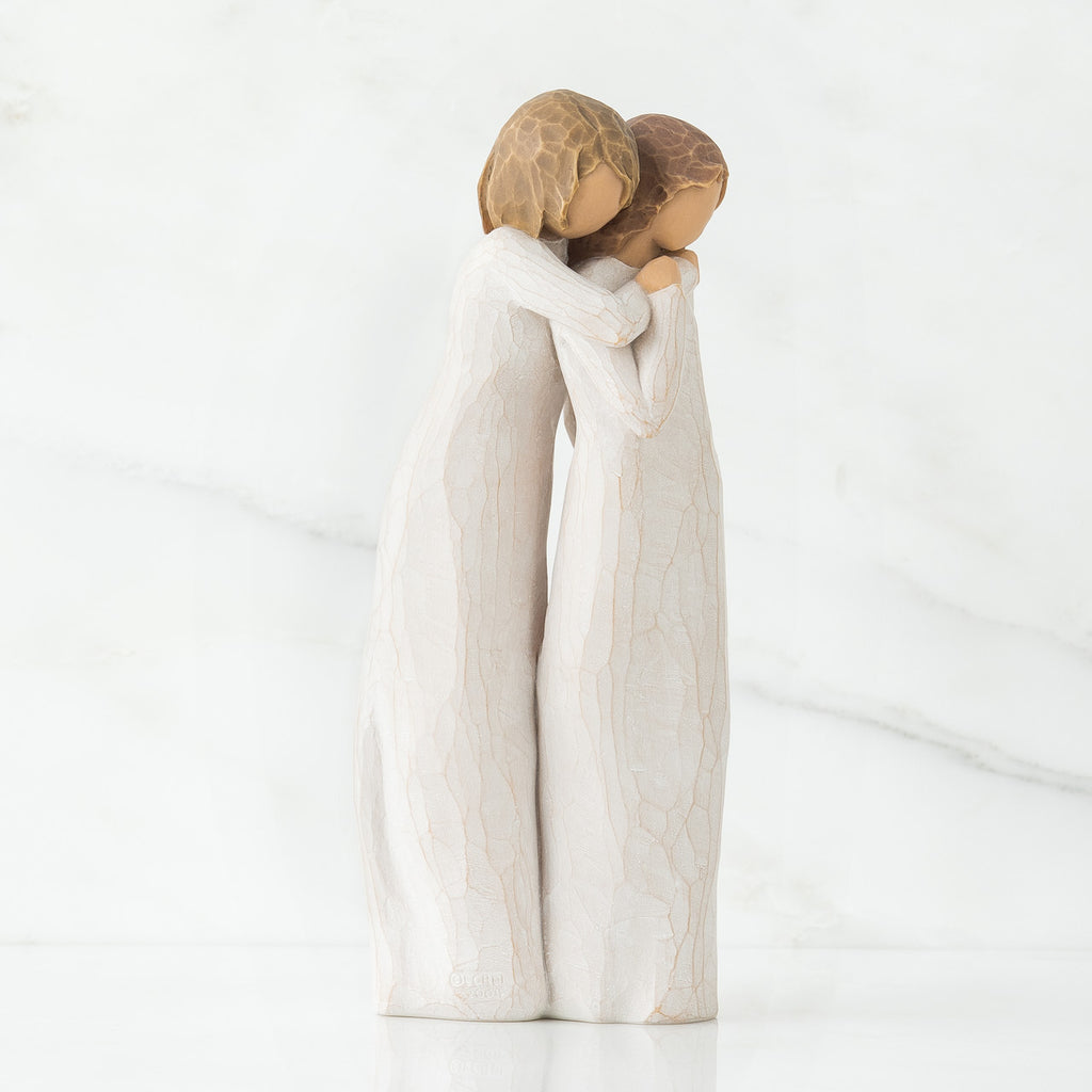 Two woman figurines in white dresses hugging one another facing the side