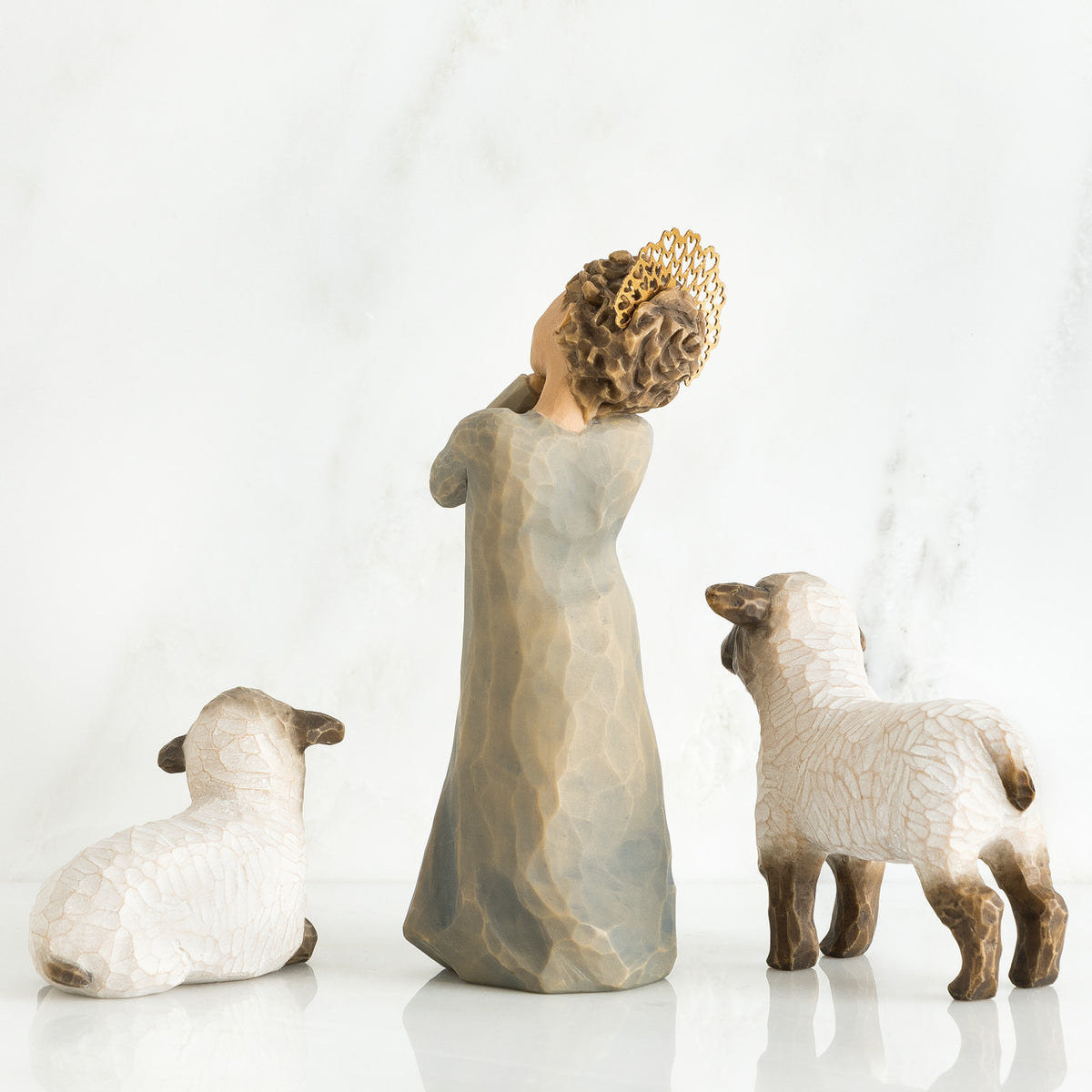 Small girl figurine wearing grey dress facing away from the camera in between two white sheep figurines