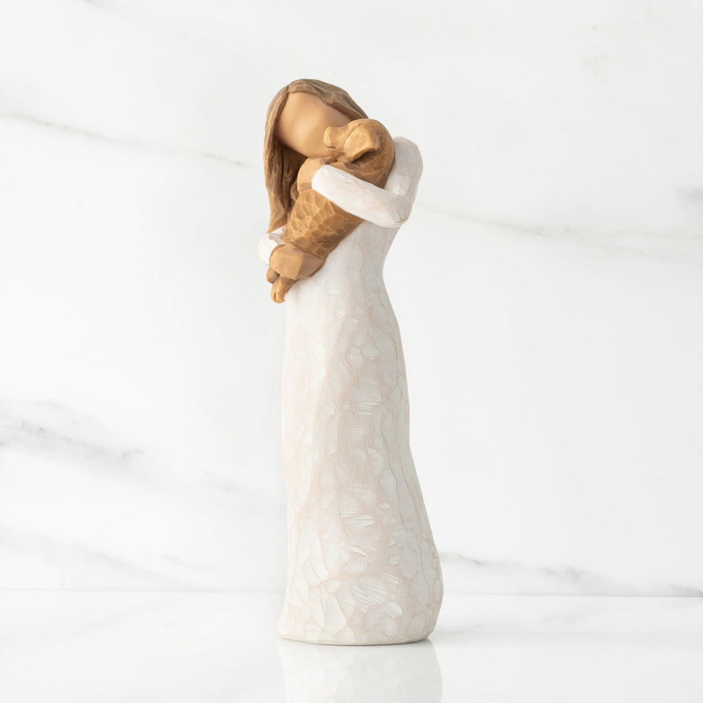 Left view, standing female figure in cream dress, holding golden color puppy in her arms