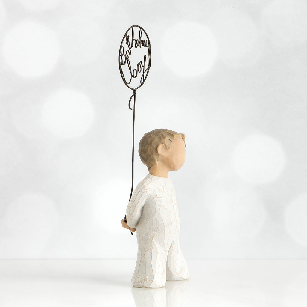Left side view of little boy with light brown hair holding a wire balloon behind his back. Text on balloon is wire