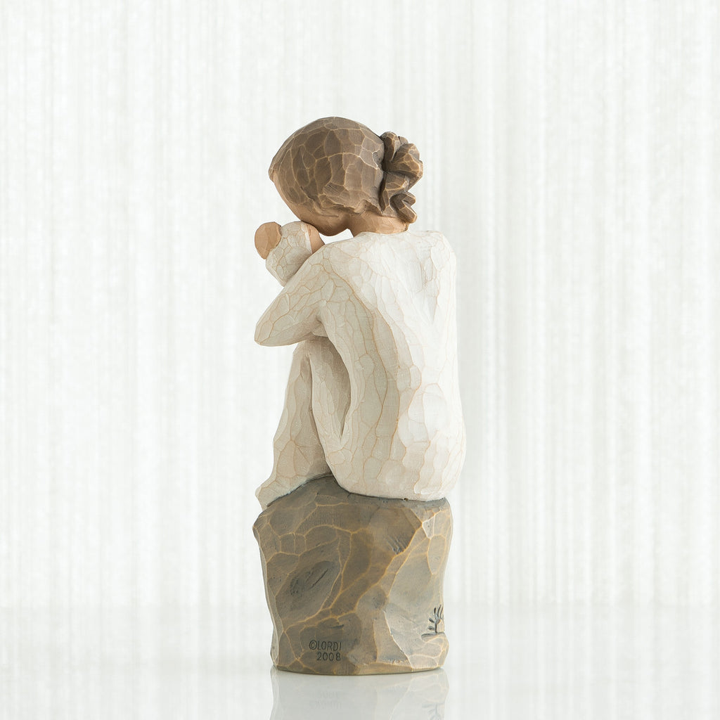 Back view of brunette girl sitting down on a rock wearing white shirt holding a baby