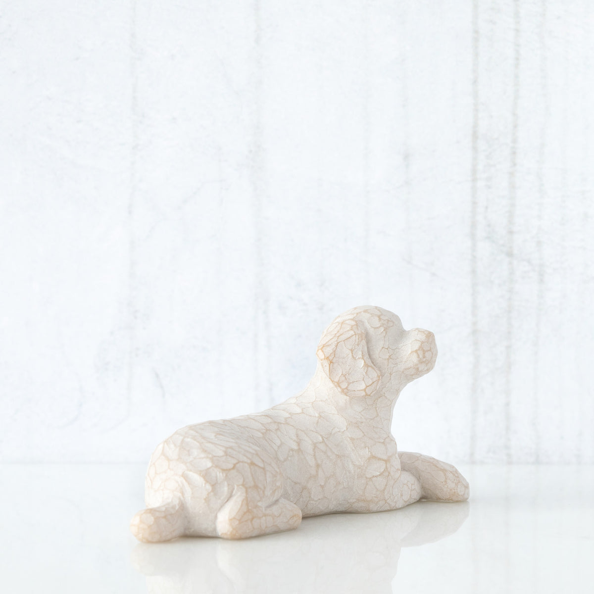 Figure of small white dog laying down with paws crossed in front, facing right