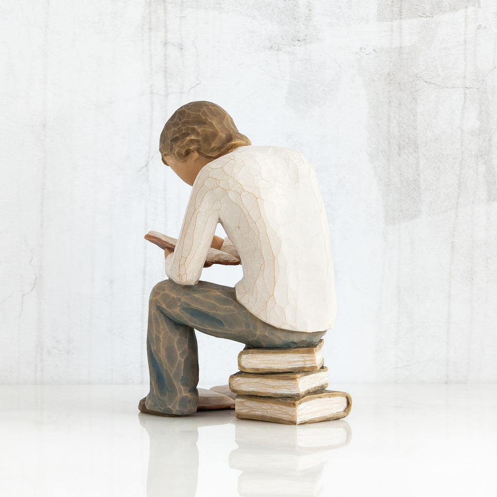 Back view of brunette man figurine in white shirt and blue jeans sitting on books reading a book