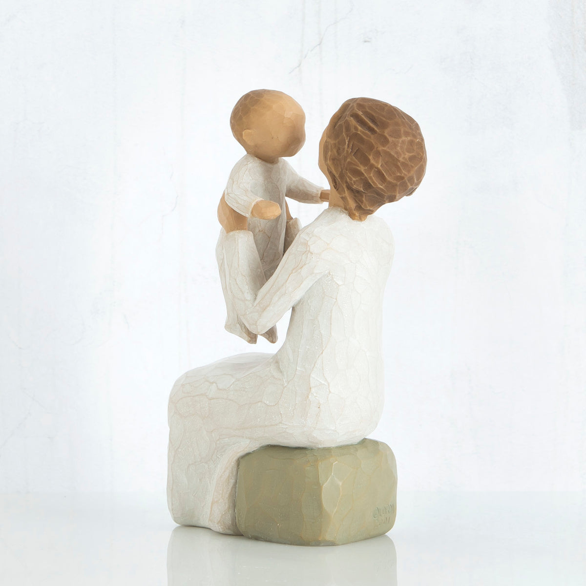 Brunette woman sitting in white on a rock holding up baby figurine