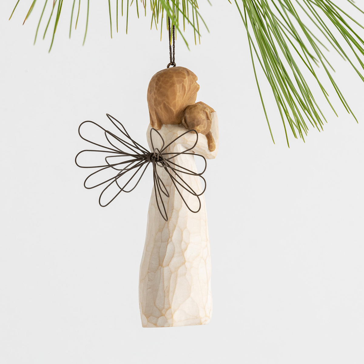 Side view female angel figure in cream dress with wire wings, holding brown dog in arms, ornament loop attached to head