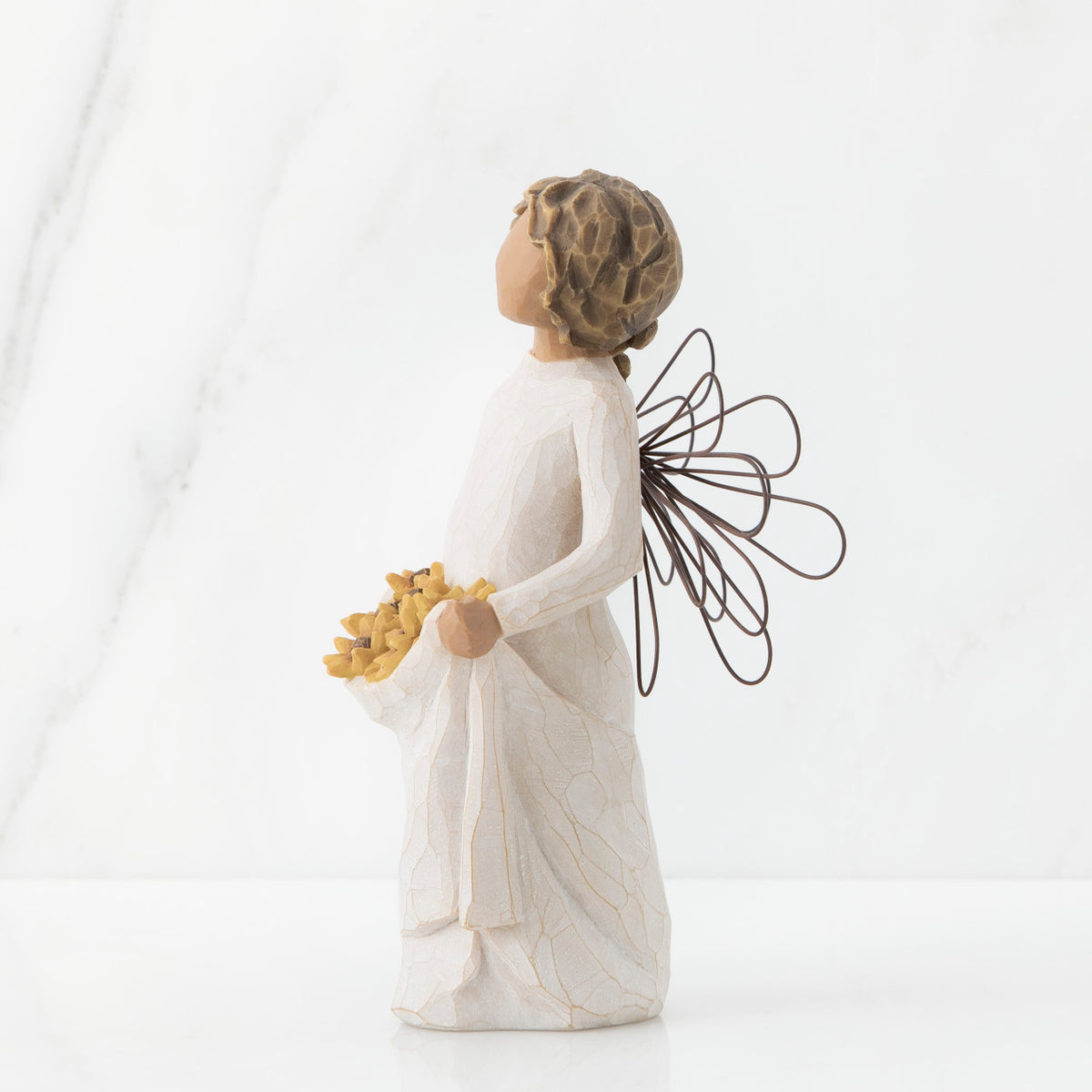 Right side view of angel with tied back, curly, dark brown hair holding up a portion of her dress's skirt as it is full of sunflowers