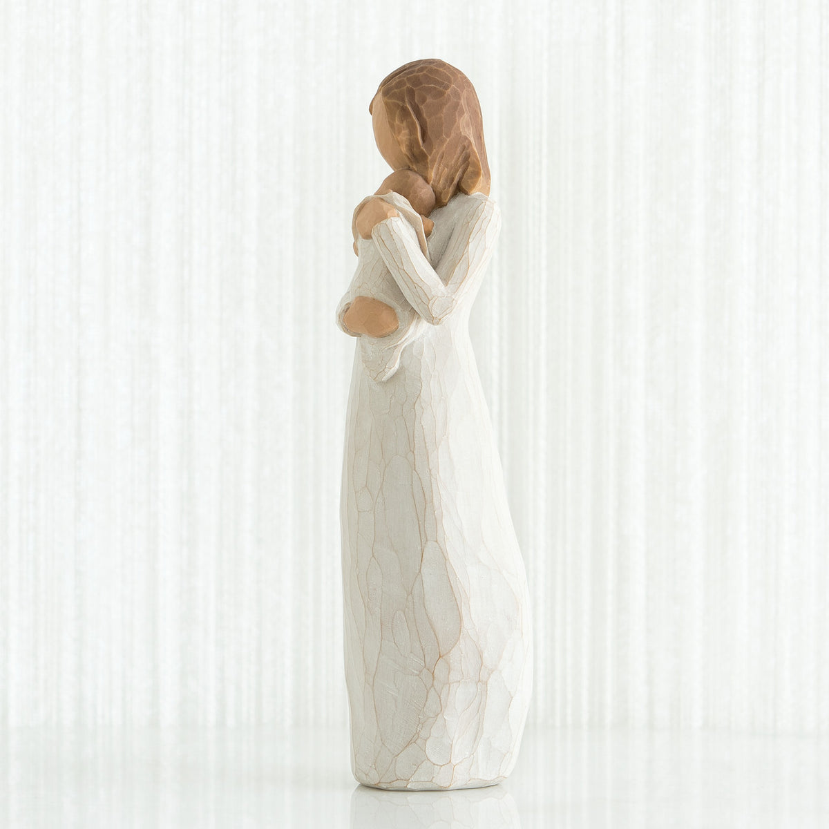 Side view of brunette girl figurine in white dress holding baby