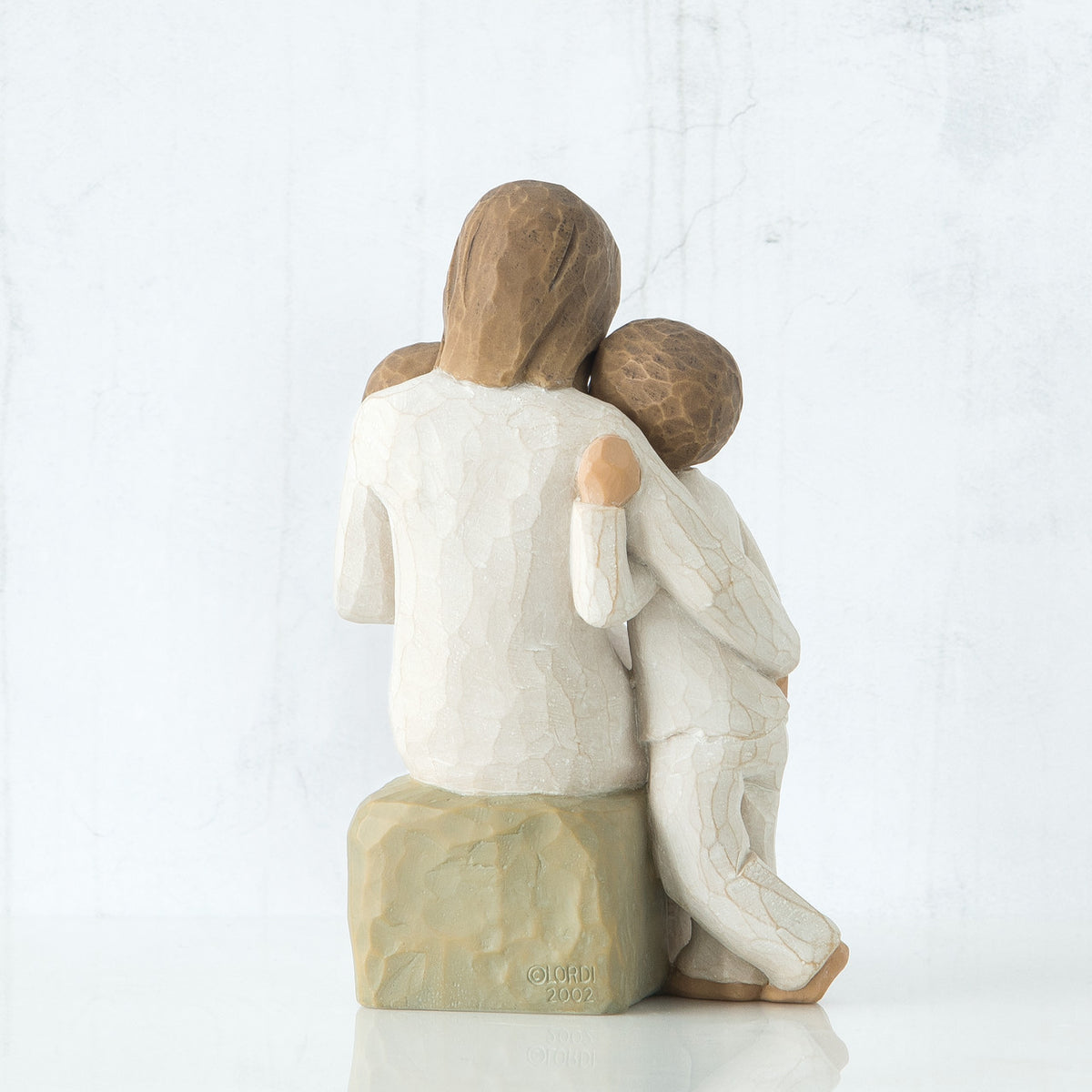 Back view of mother figurine holding young boy figurine - sitting on rock