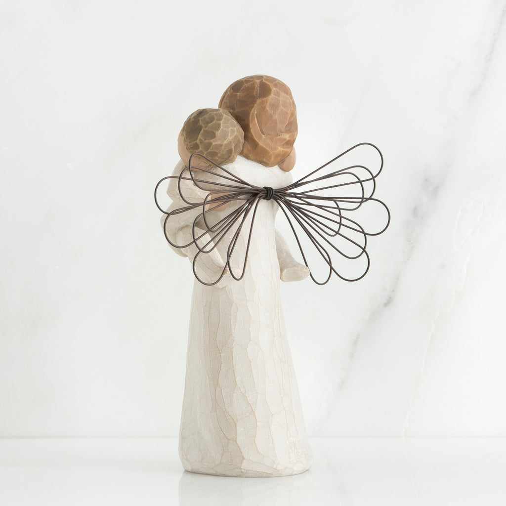Back view of brunette girl figurine in white dress with brown wings holding baby