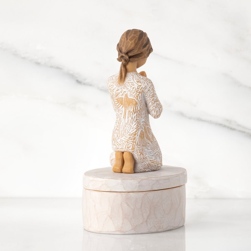 Back view: cream oval resin box, 3-D figure in prayer pose atop lid, in cream dress carved with birds and flowers