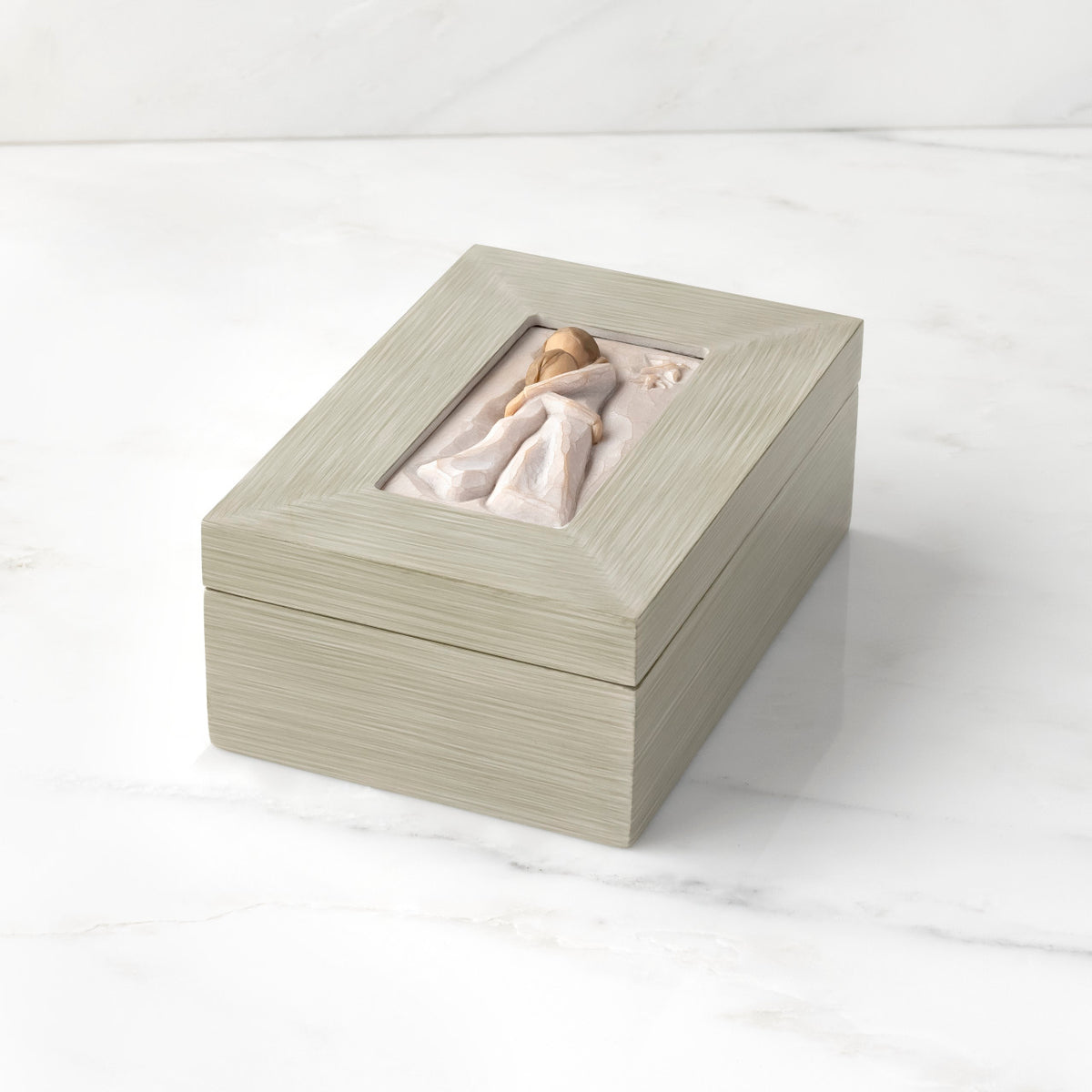 Top down view: Light gray rectangular wood box with hinged lid, carving on lid of female and child embracing in cream dresses