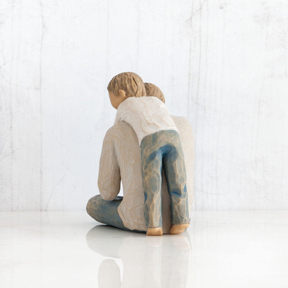 Back view of little boy figurine in blue jeans and white shirt hugging a larger father figurine