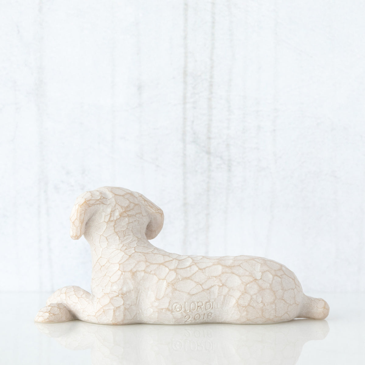 Figure of small white dog laying down with paws crossed in front, facing back
