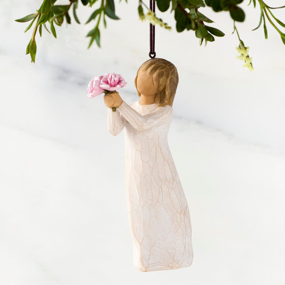 Front view of female figure in cream dress holding out small bouquet of pink peonies, ornament loop affixed to top of head