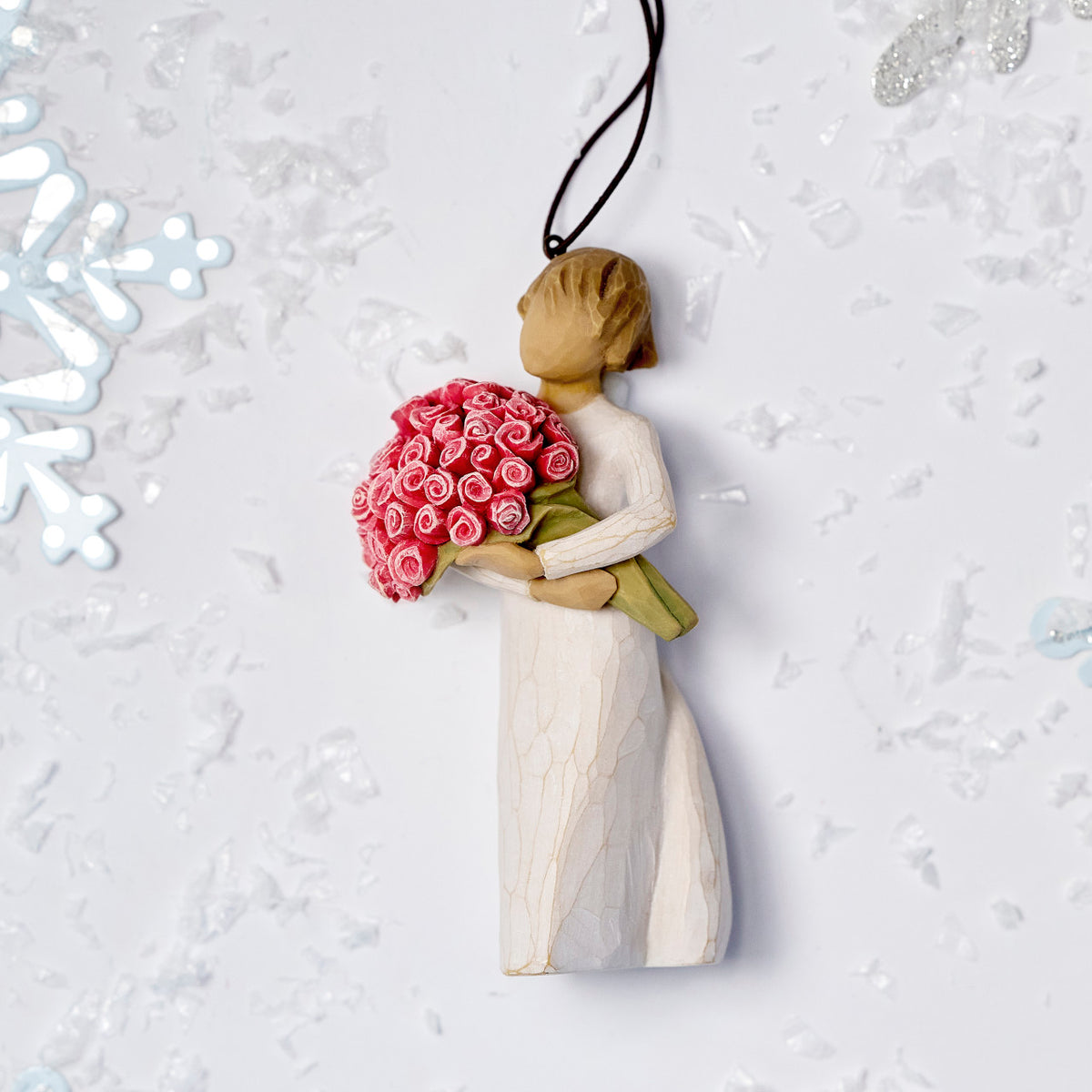 Willow Tree Abundance Ornament, 4”h hand-painted resin figure in cream dress, holding bouquet of pink roses, brown elastic cord, laying amongst snowflakes