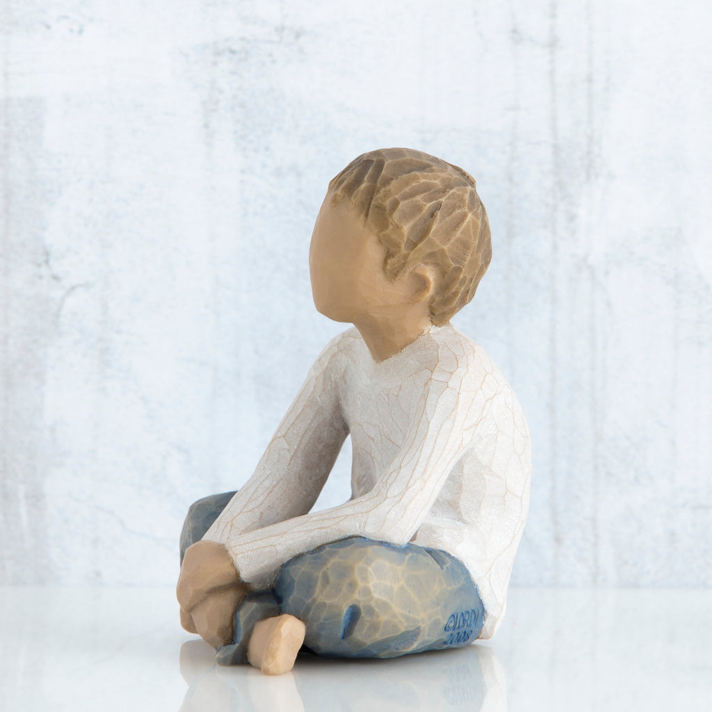 Young brunette boy figurine in white shirt and blue jeans sitting down