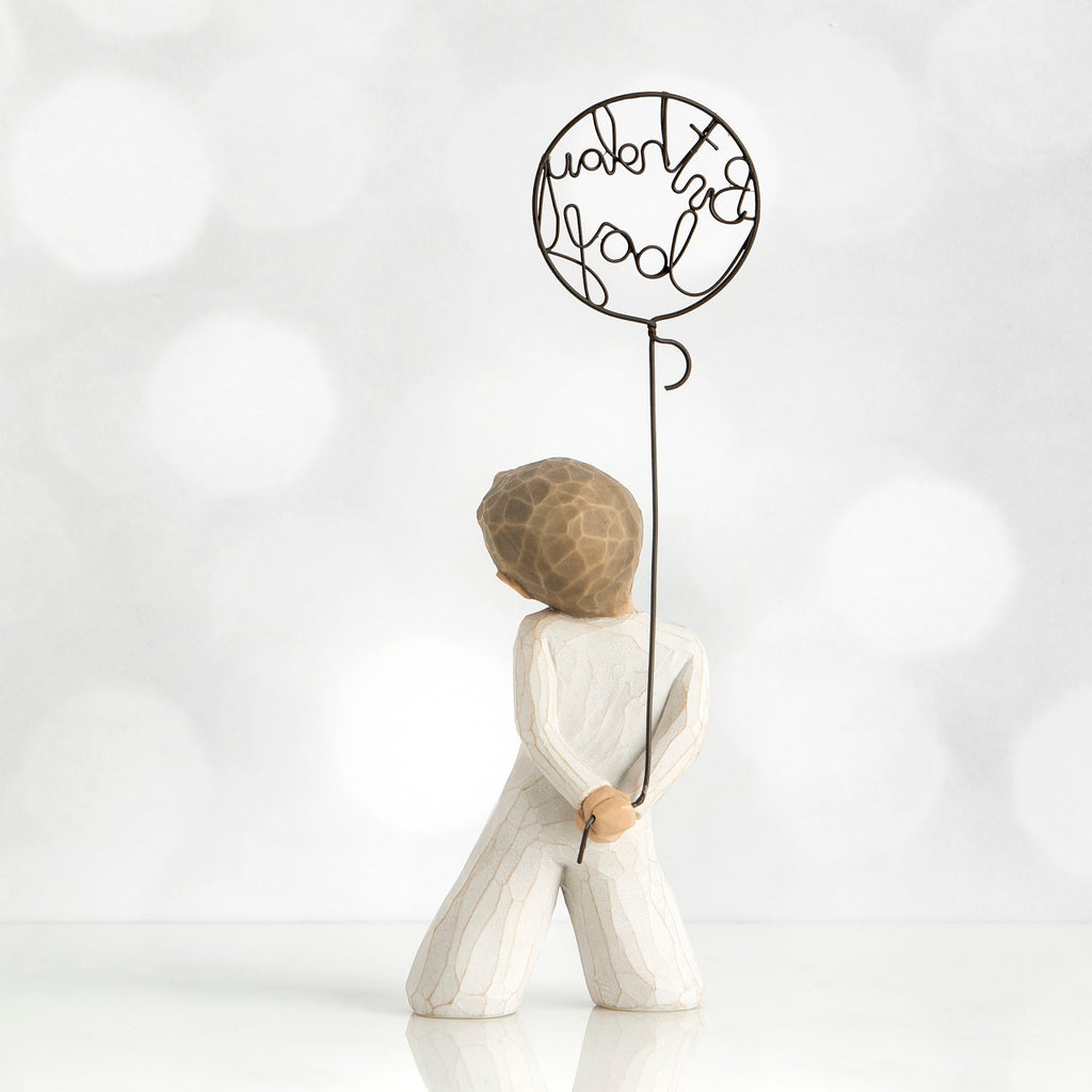 Back view of little boy with light brown hair holding a wire balloon behind his back. Text on balloon is wire