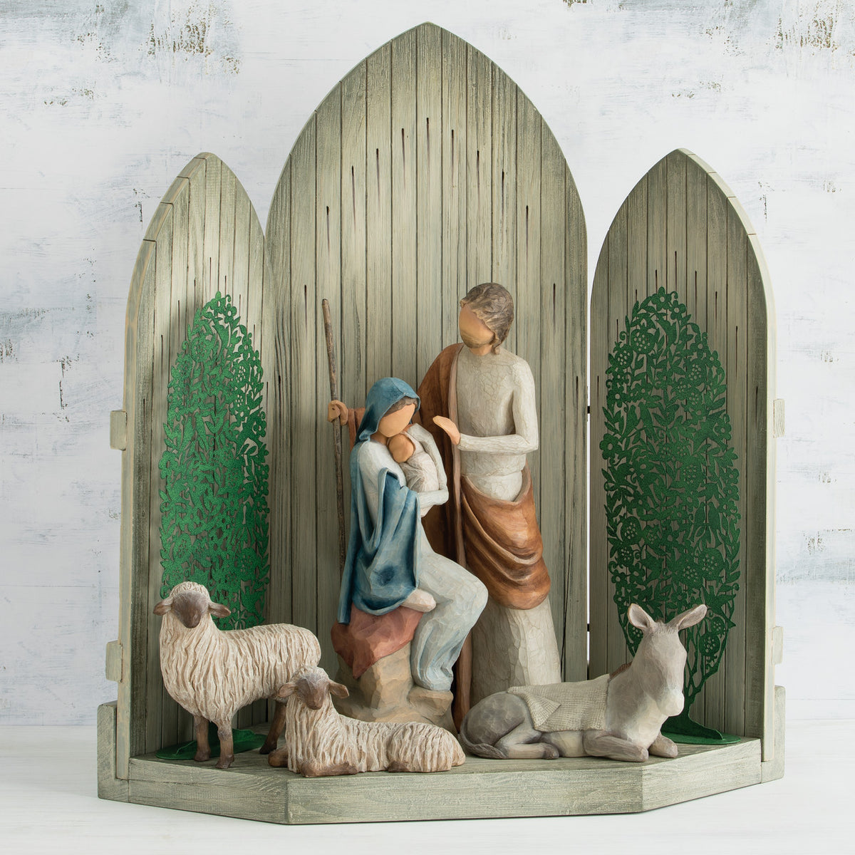 Light grey barn figurine with open doors, man and woman figurines in the center holding baby, two white sheep surrounding them