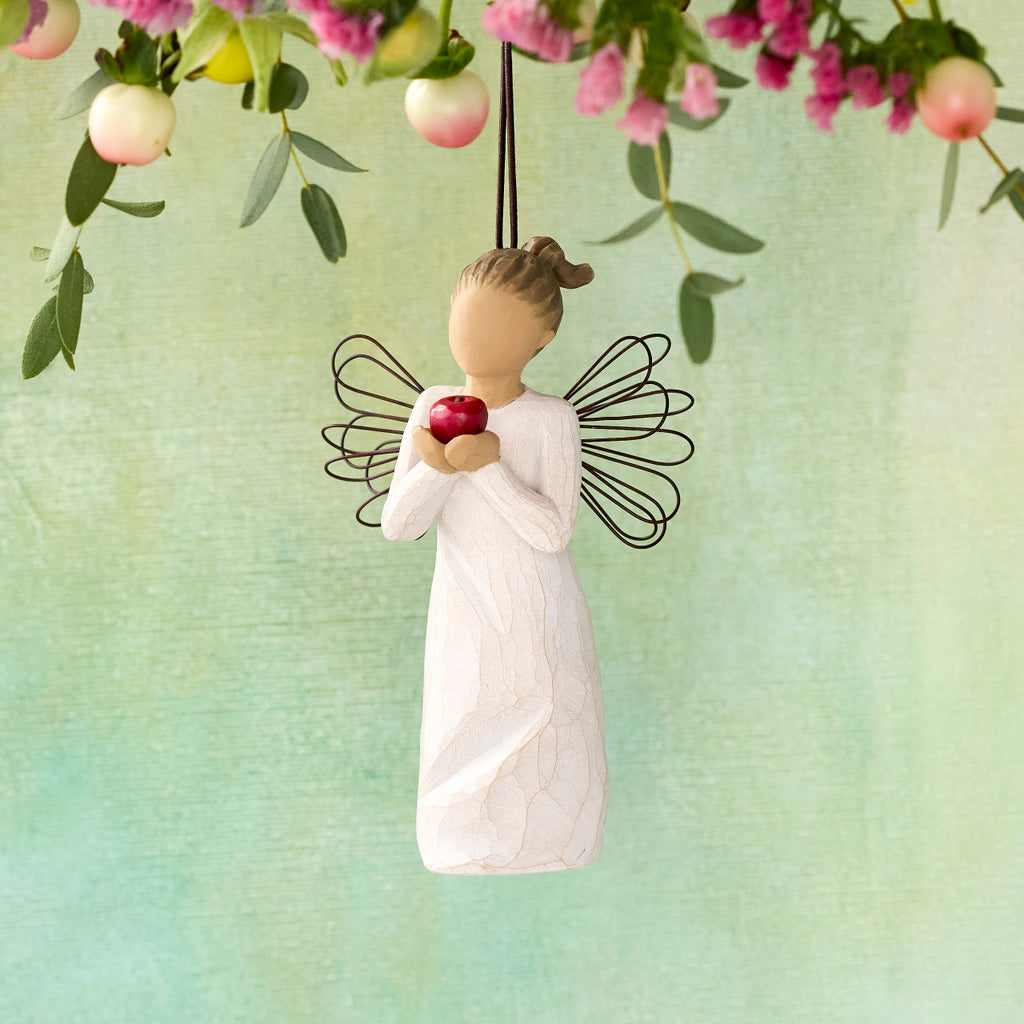 Willow Tree You're the Best! Ornament, 4.5"h hand-painted resin figure in cream dress with wire wings, holding red apple, brown elastic cord, hanging in front of yellow-green painting