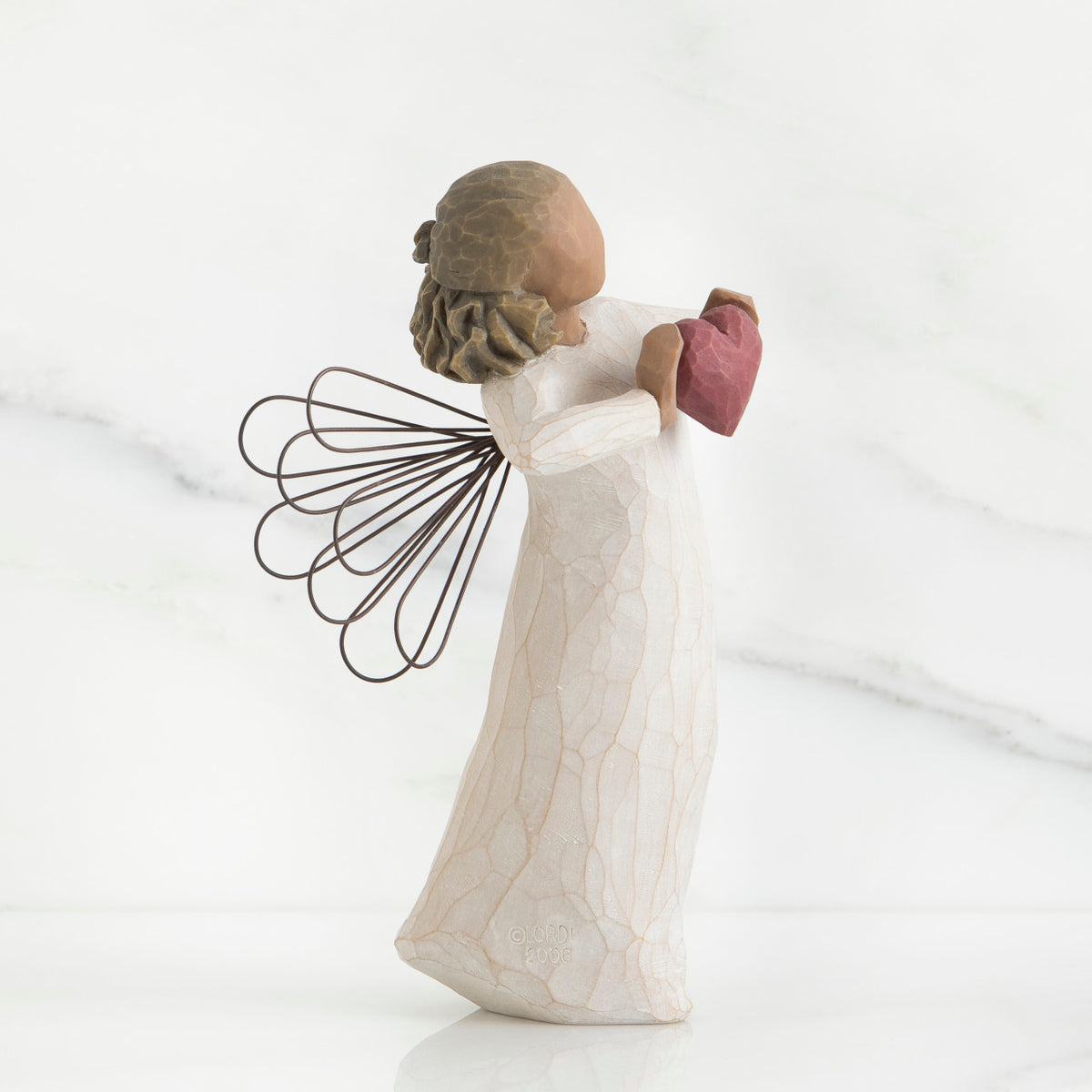 Side view of brunette angel girl figurine in white dress holding pink heart figurine