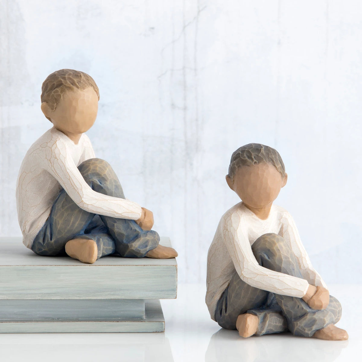 Two young boy figurines sitting down in white shirts and blue jeans