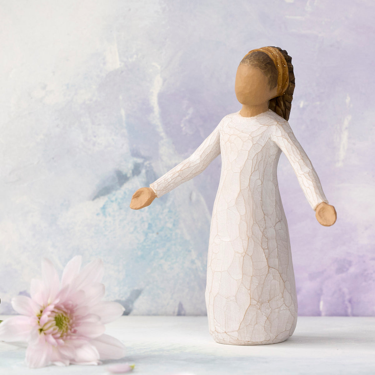 Willow Tree Blessings, 5.5”h hand-painted resin figure in cream dress with darker skin and hair, wearing glitter headband, arms stretched out to sides, in front of light purple painting