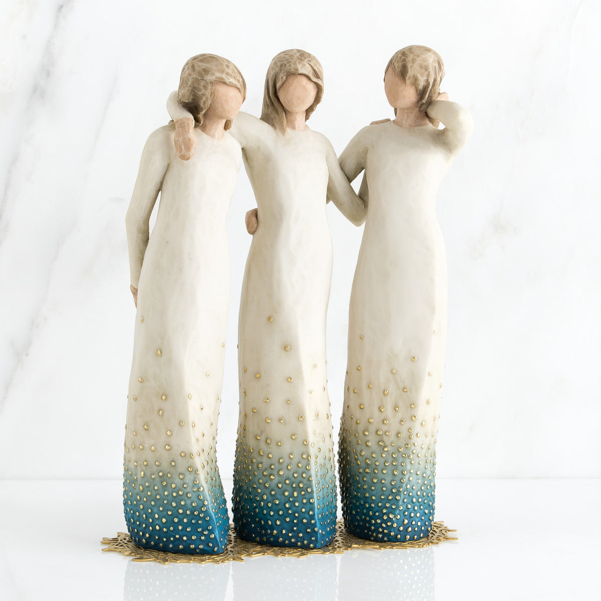 Three brunette woman figurines in white dresses blue bottoms facing forward with arms around each other