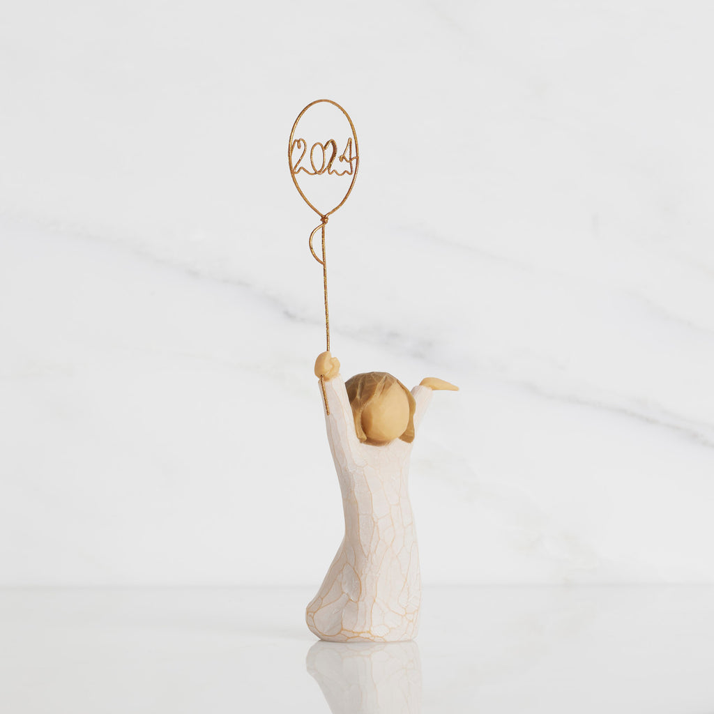 Facing right: standing figure in cream dress, arms raised, holding gold wire balloon with 2024 written in gold wire inside