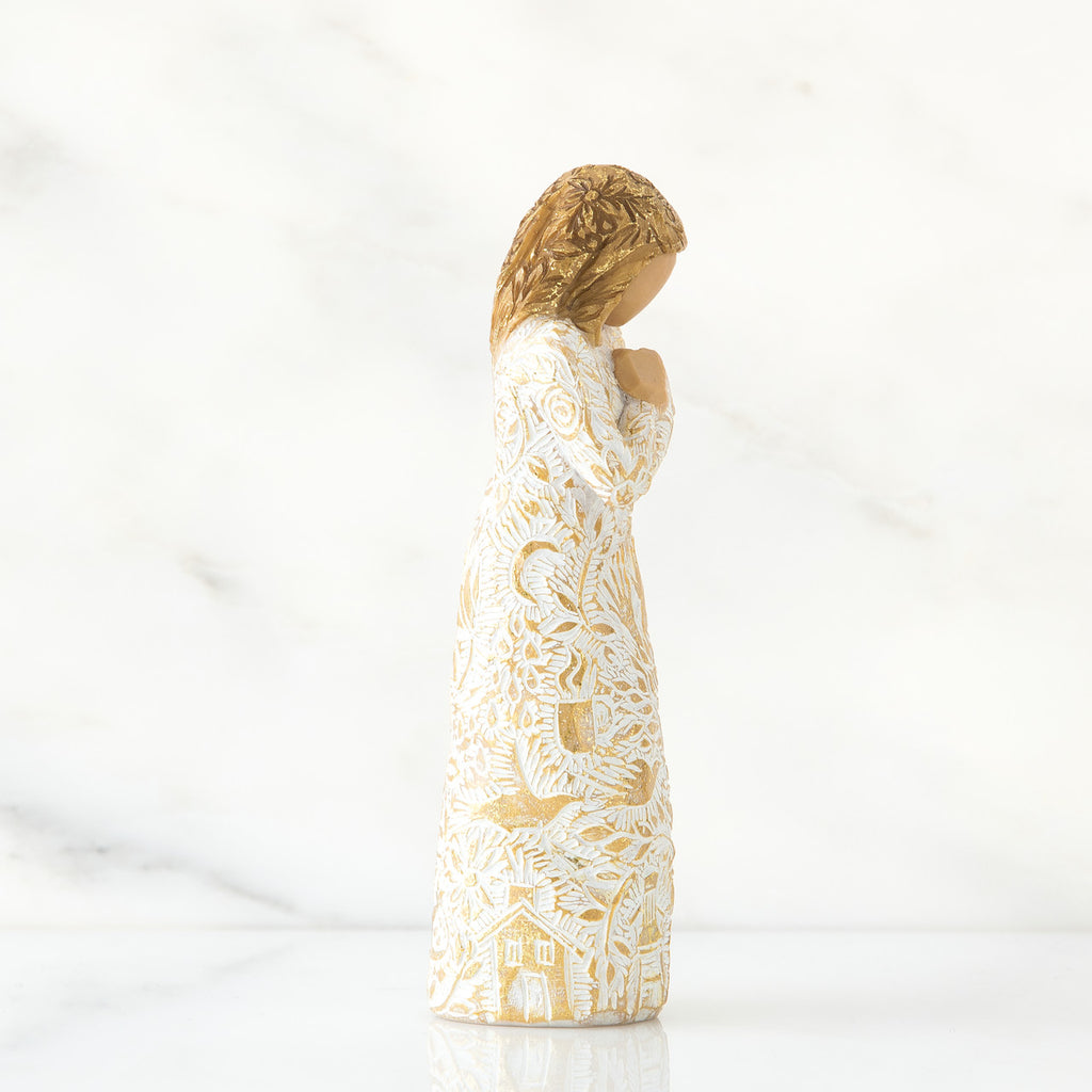 Gold haired girl figurine in white / gold dress facing the side holding her hands to her chest - white background